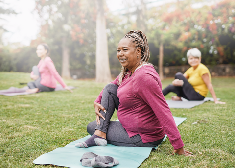 Elderly woman sitting on yoga mat outside.